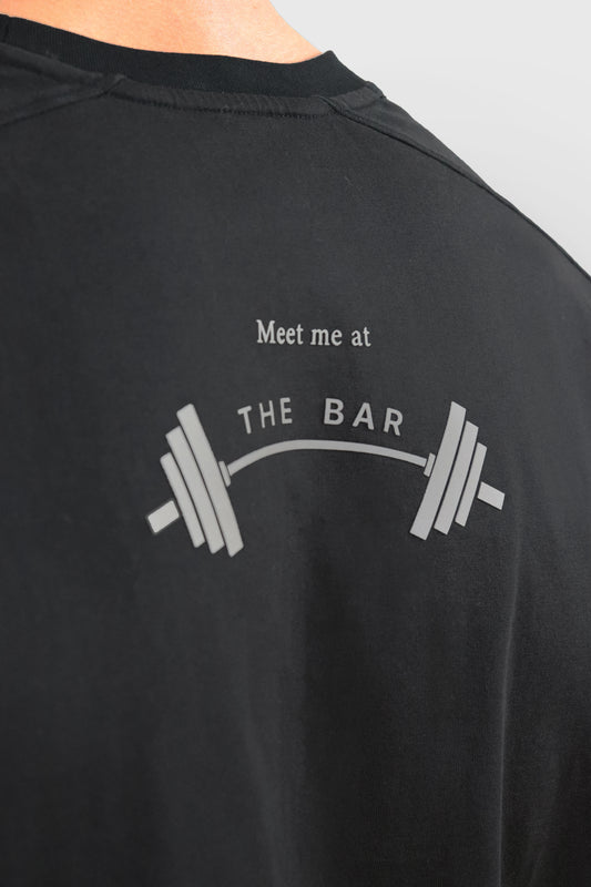 Black cotton t-shirt with a graphic and text 'Meet me at THE BAR' and a barbell on a plain background