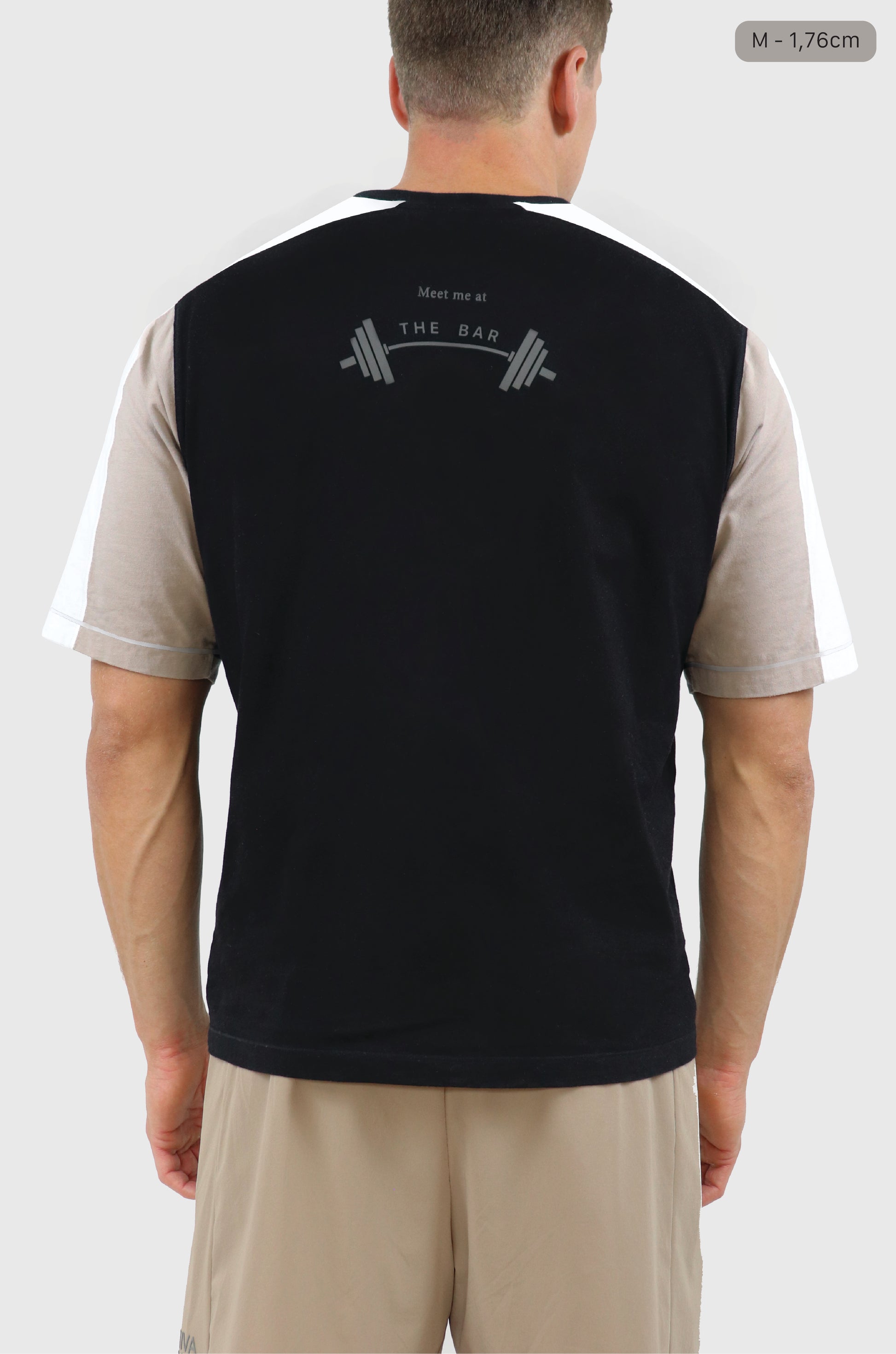 Man wearing cotton black, beige and white t-shirt with raglan sleeves, grey 'meet me at the bar' with barbell graphic print at back, beige shorts, white background.