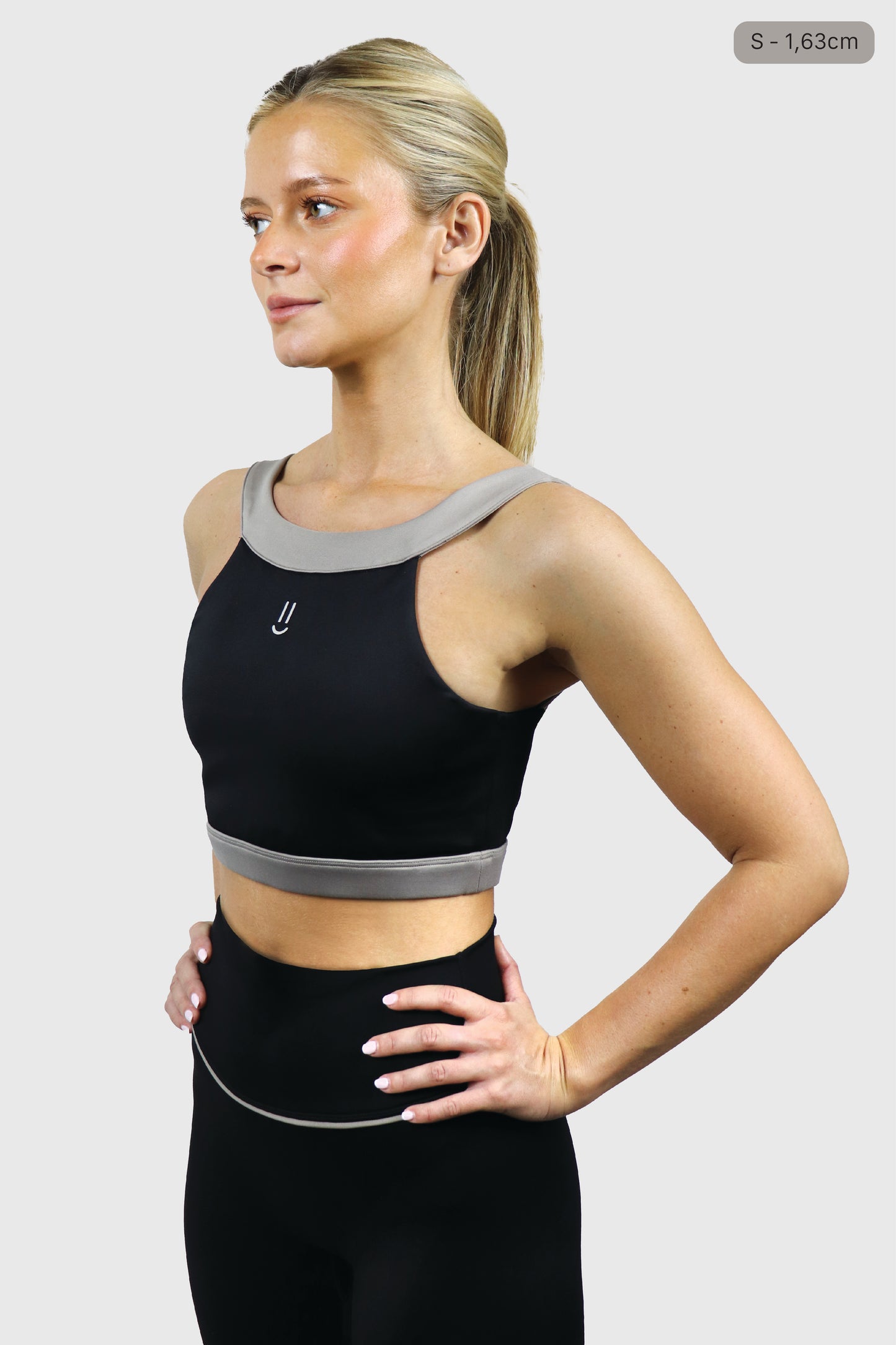 Woman wearing a black athletic top with small smiley print at front and leggings with gray taupe accents on a white background