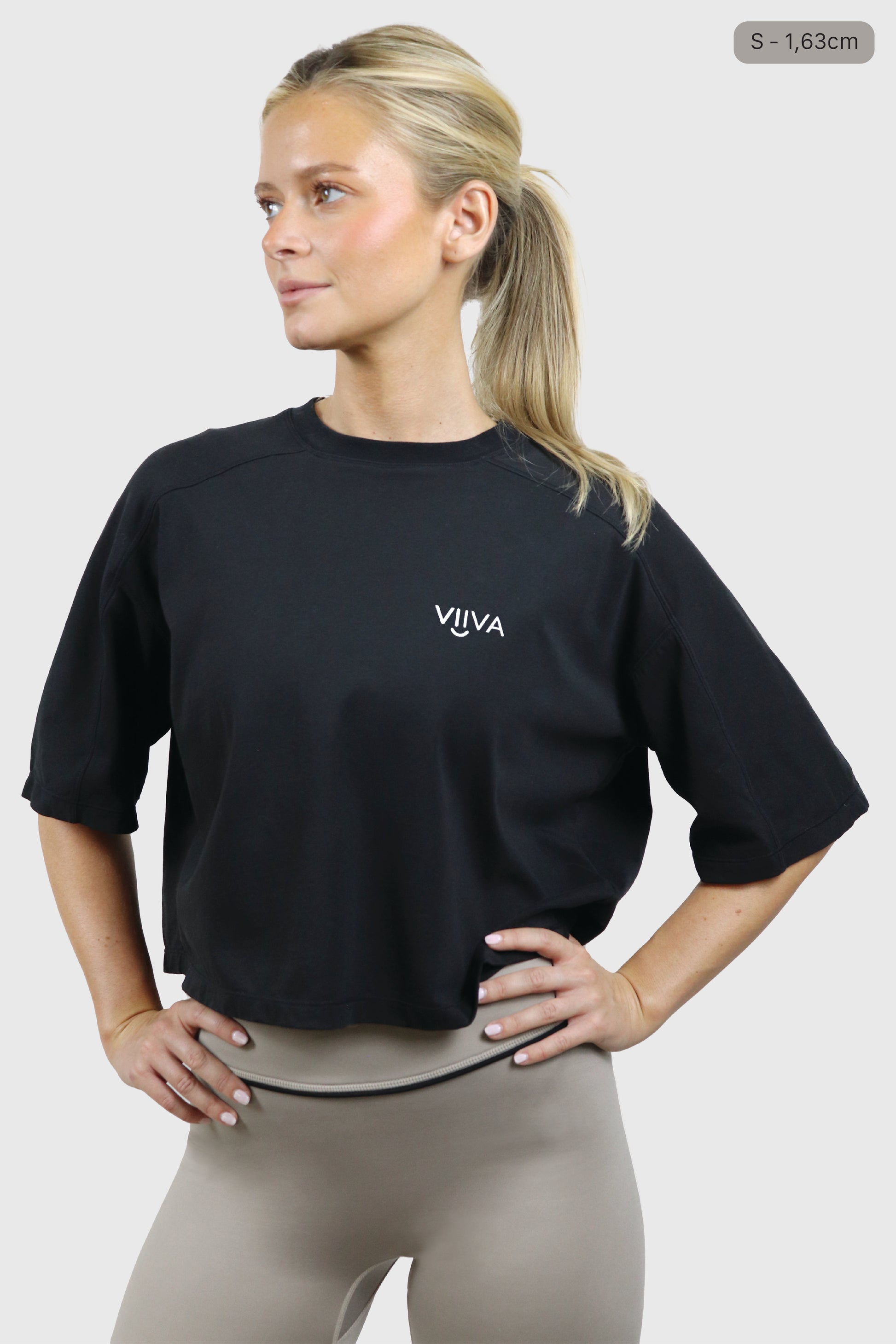 Woman wearing a black cotton t-shirt and taupe leggings with VIIVA text in white on a white background