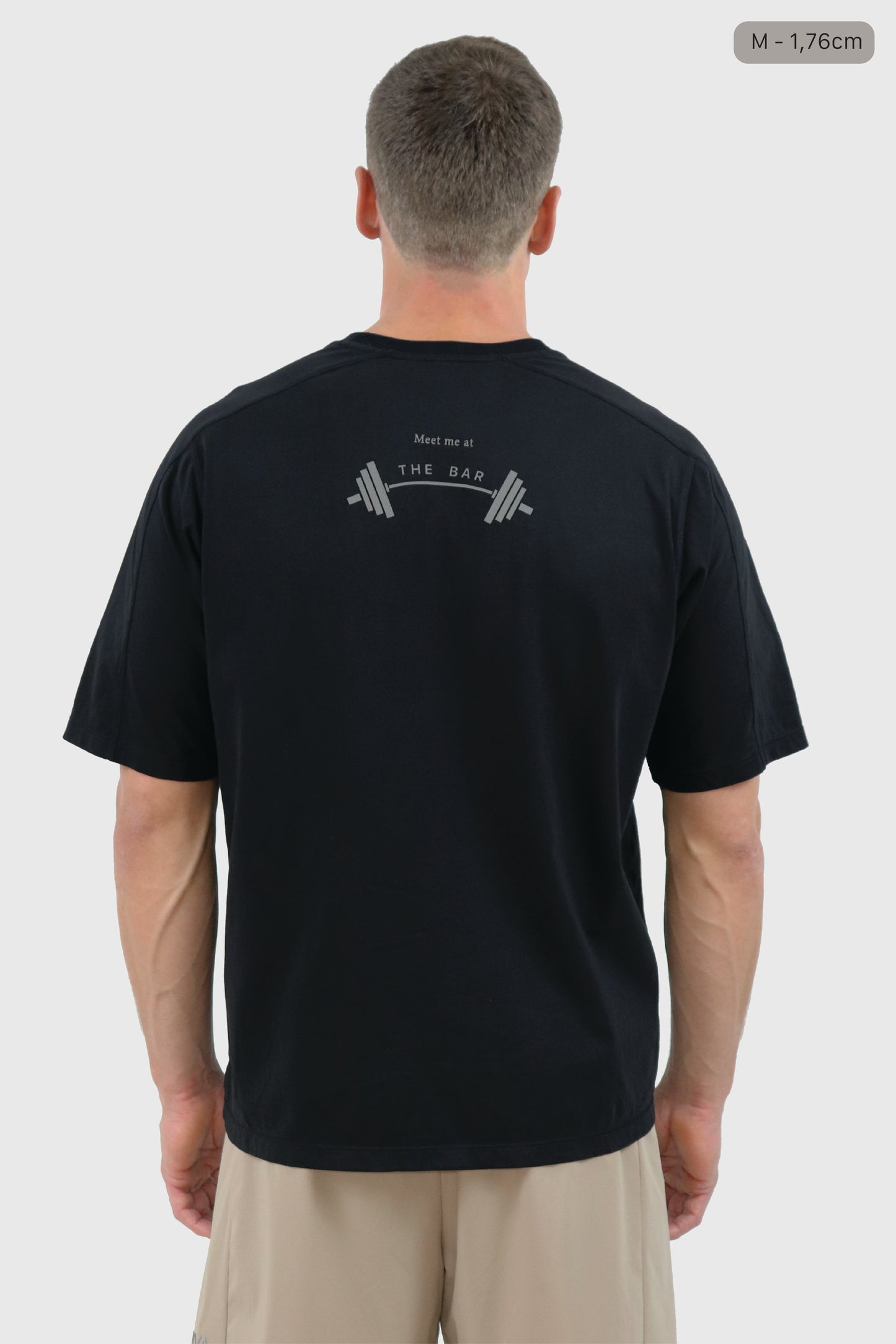 Man wearing a black cotton t-shirt with a print 'Meet me at the bar' on the back against a white background