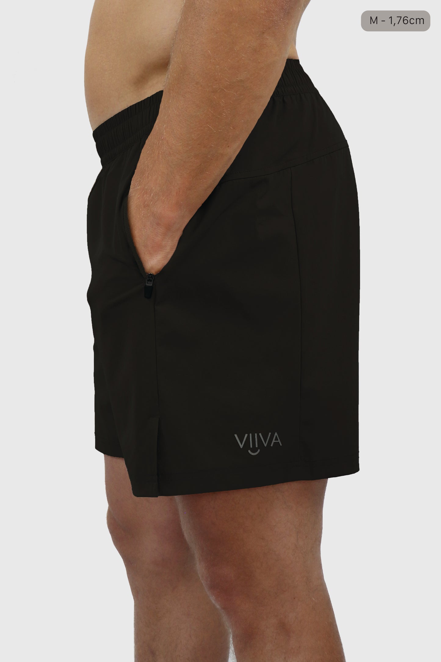 Black men's shorts with elastic waistband and small VIIVA logo print, hands in the pocket worn by a person on a white background