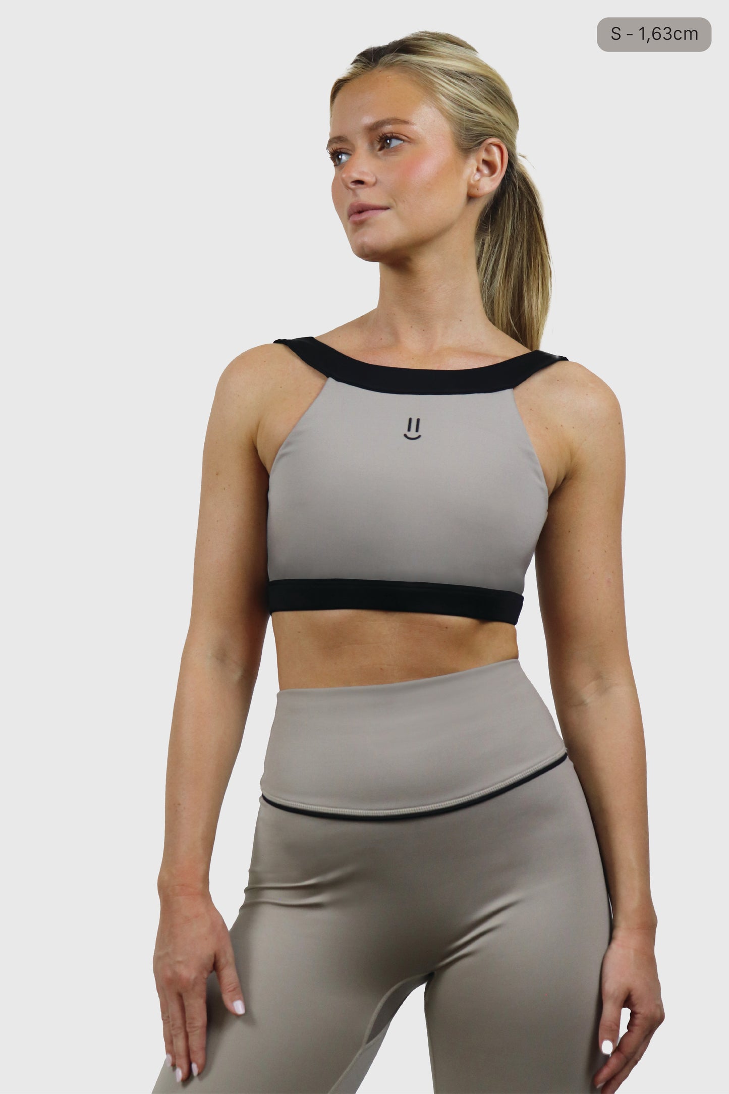 Woman wearing a beige taupe sports bra and taupe leggings with black accents on a white background