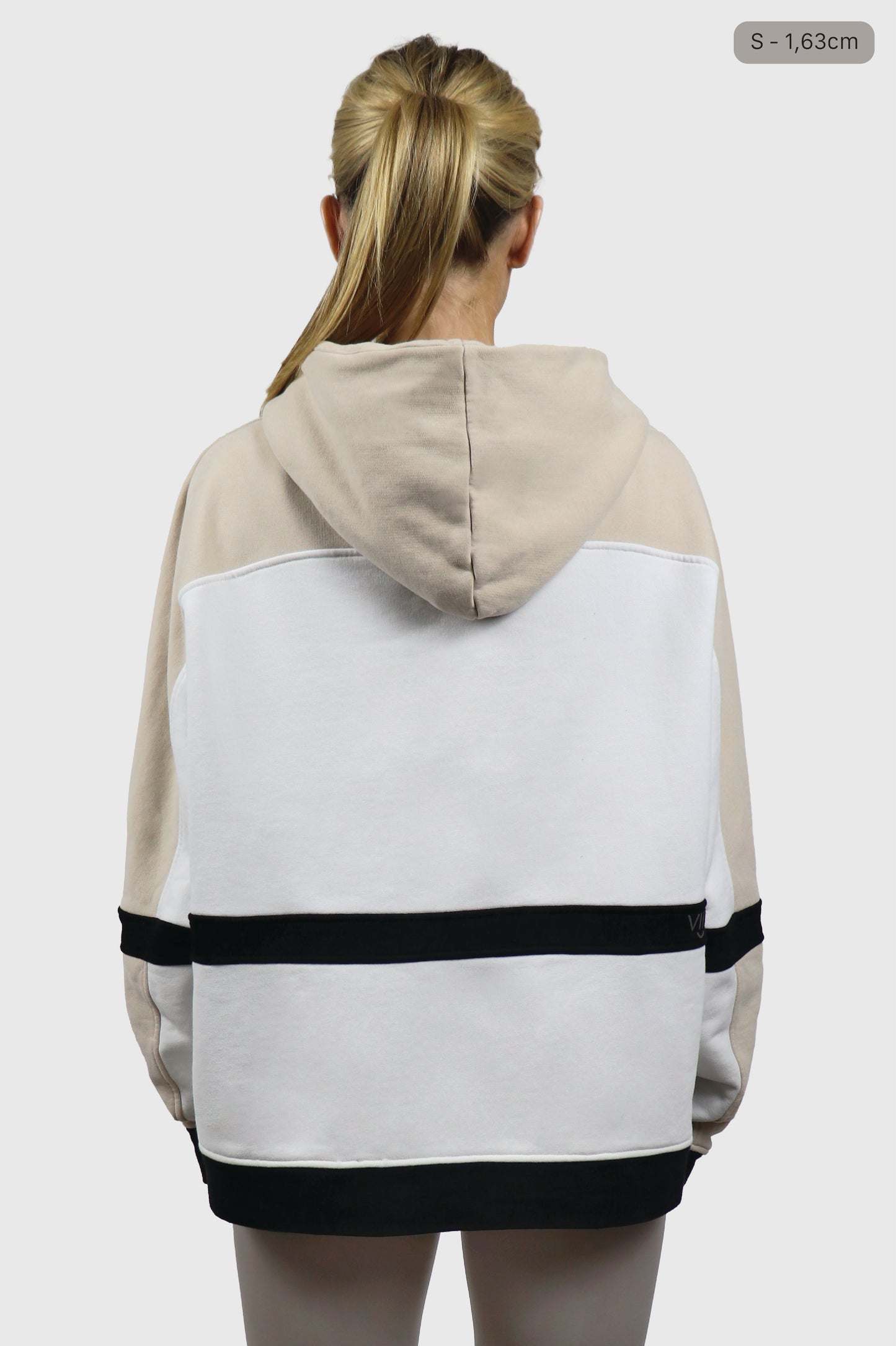 Woman wearing a beige and white hoodie with black stripes on a plain background