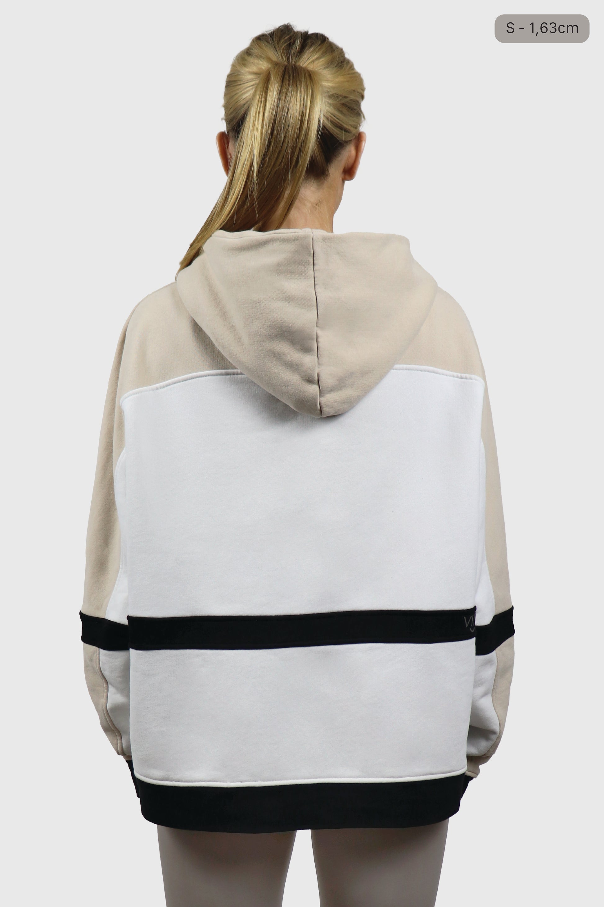 Woman wearing a beige and white hoodie with black stripes on a plain background