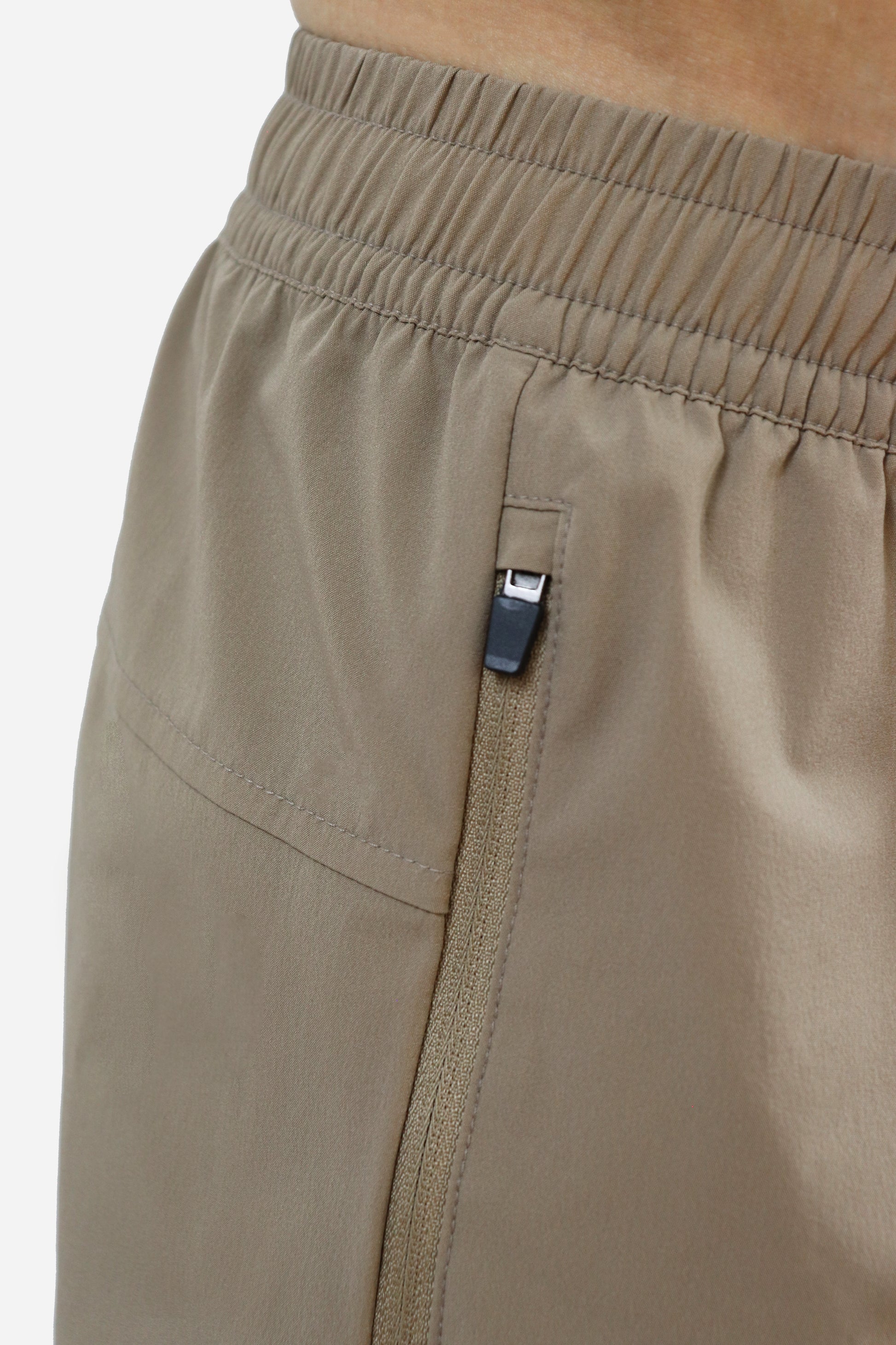 Close-up of beige shorts with elastic waistband and a zipper pocket on a white background