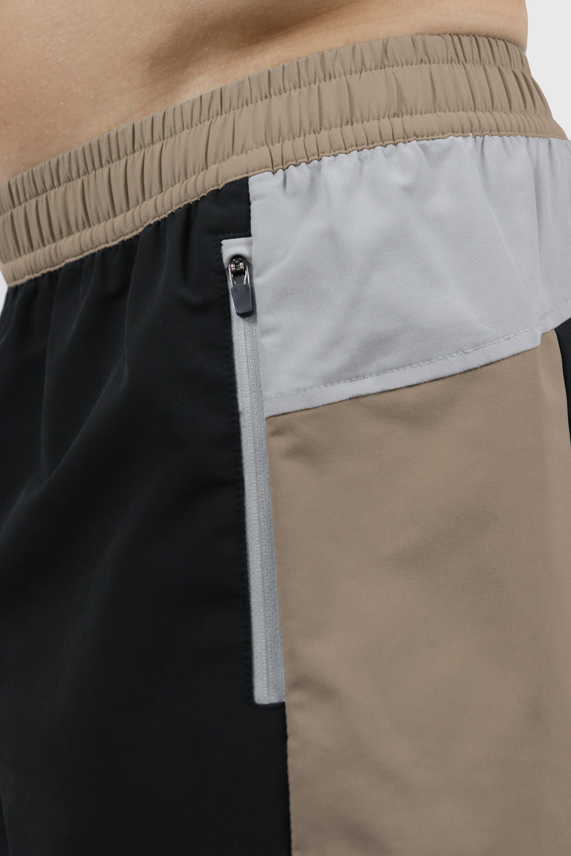 Close-up of men's shorts in white, black and beige, with beige elastic waistband, with a zipper pocket.