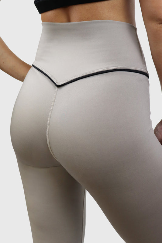 Beige taupe leggings with a black piping detail at waistband on a neutral background