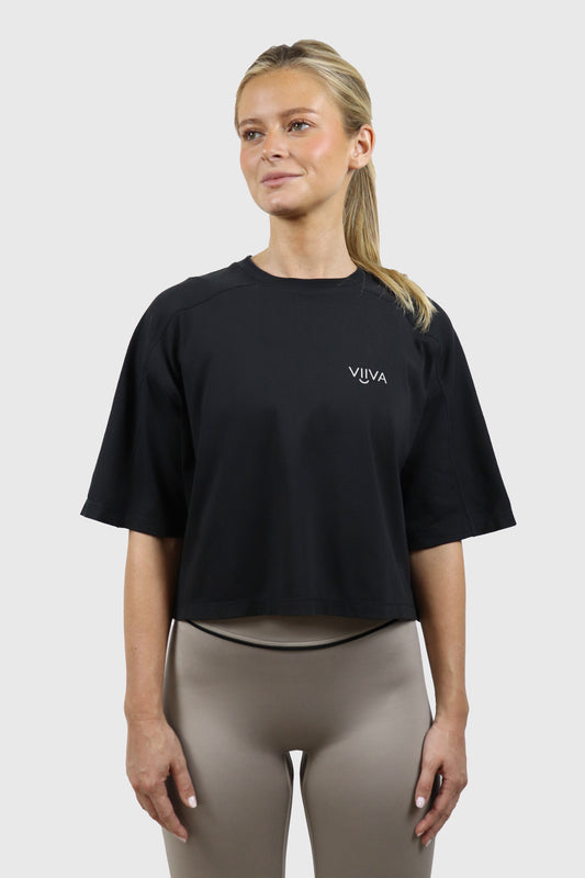 Woman wearing a black cotton t-shirt and taupe leggings with black detail with 'VIIVA' logo on a white background
