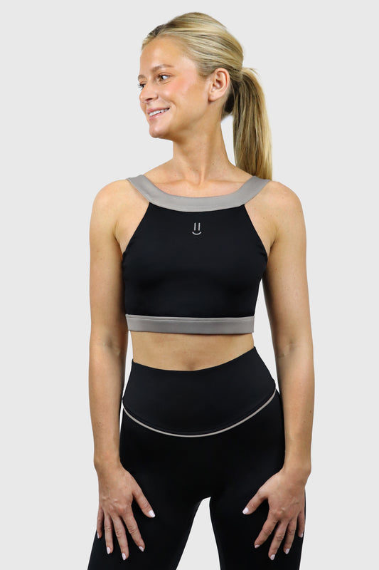 Woman wearing a black athletic top with small smiley print at front and leggings with gray taupe accents on a white background