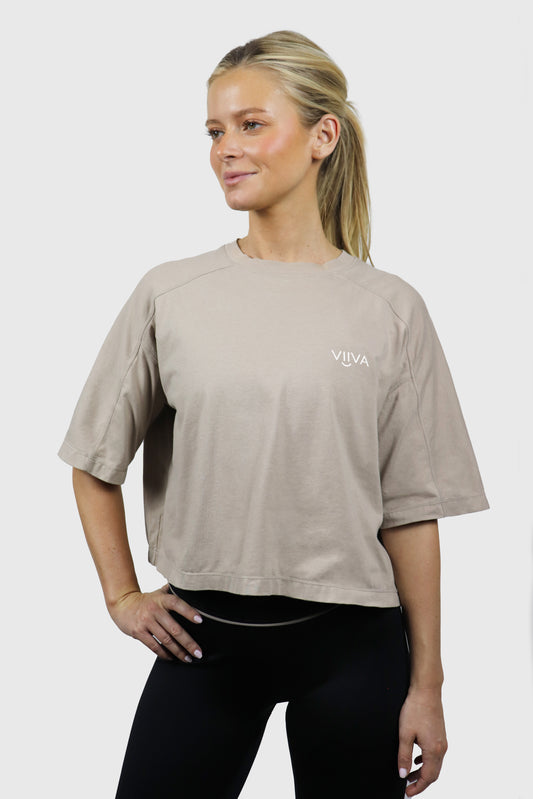 Woman wearing a beige cotton t-shirt with small logo print at front in white, standing against a white background
