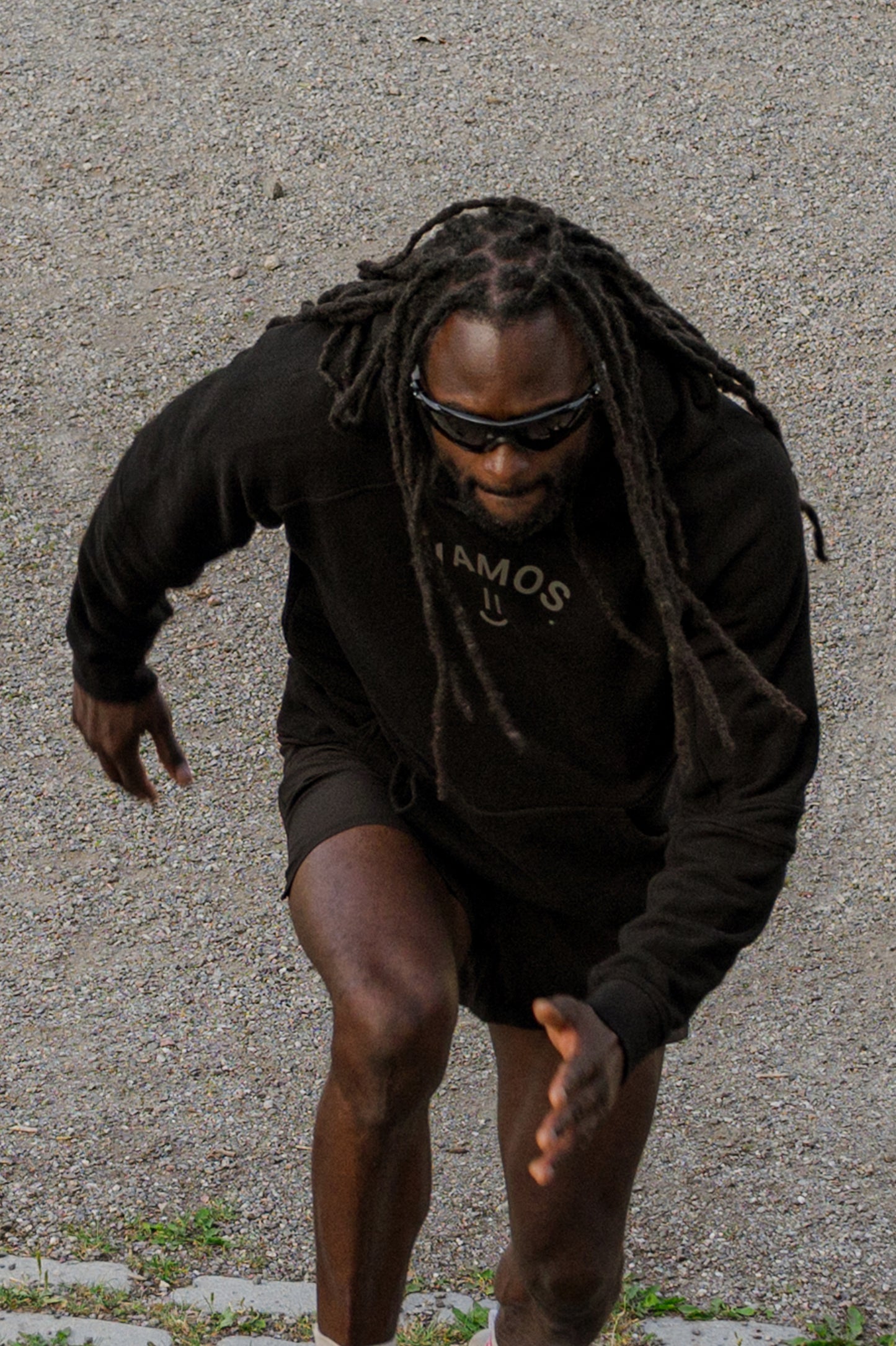 Person wearing a black hoodie and sunglasses on a textured pavement background