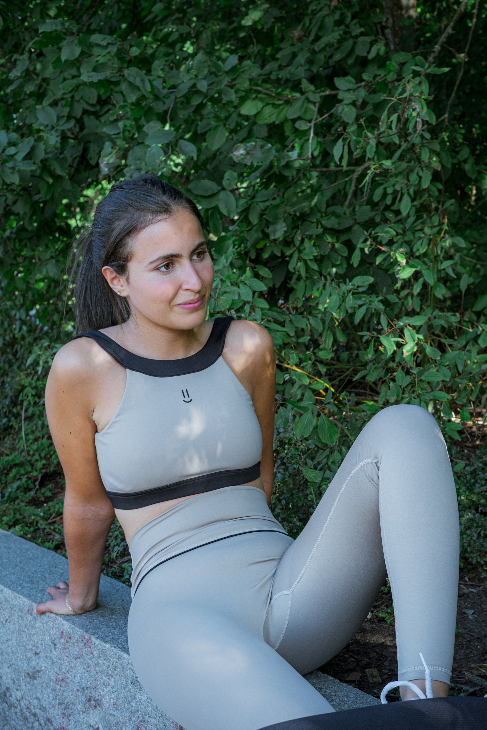 Woman wearing a beige taupe legging and top athletic outfit with black accents and details sitting on a park