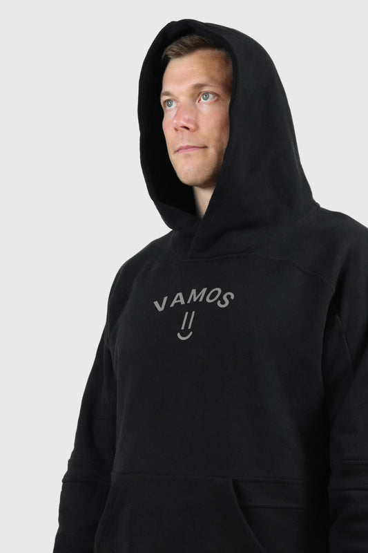 Man wearing a black cotton hoodie with 'VAMOS' print at front a white background