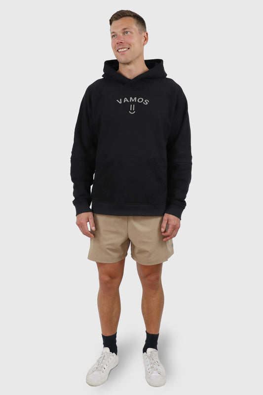Man wearing a black cotton hoodie with 'VAMOS' print at front and beige shorts on a white background