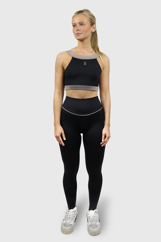 Woman wearing a black athletic top and leggings with taupe grey accents, and small smiley print at front of top