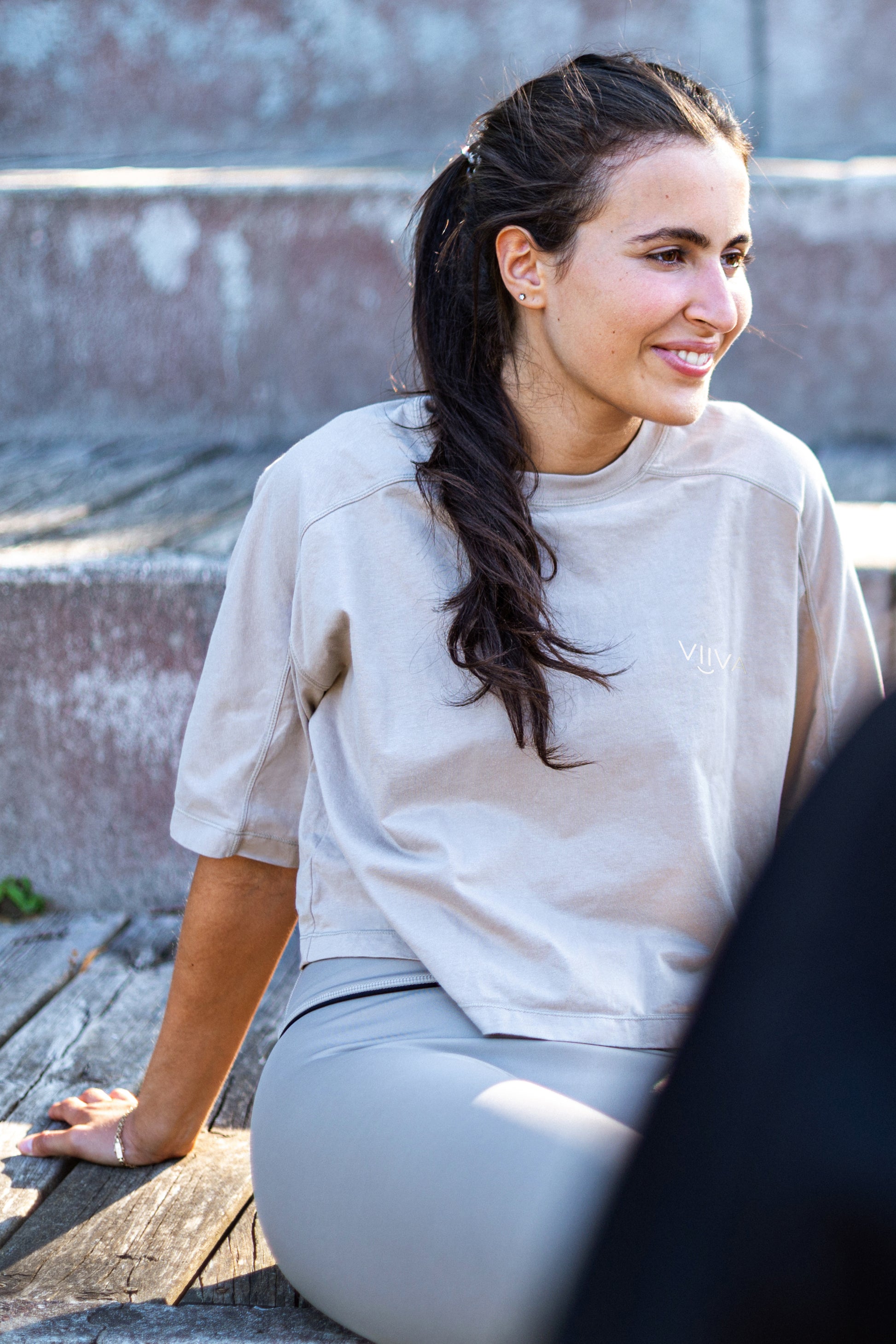 Woman sitting outdoors wearing a light-beige cotton shirt and gray leggings