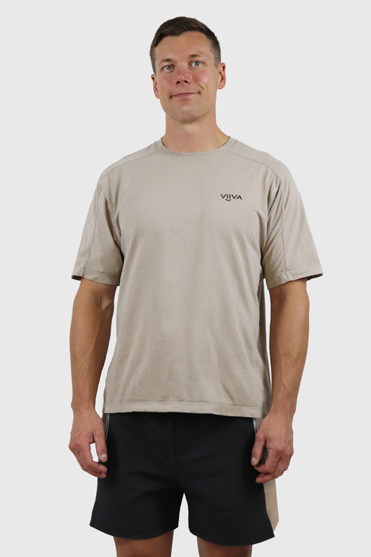 Man wearing a beige cotton t-shirt with a black logo and black shorts on a white background