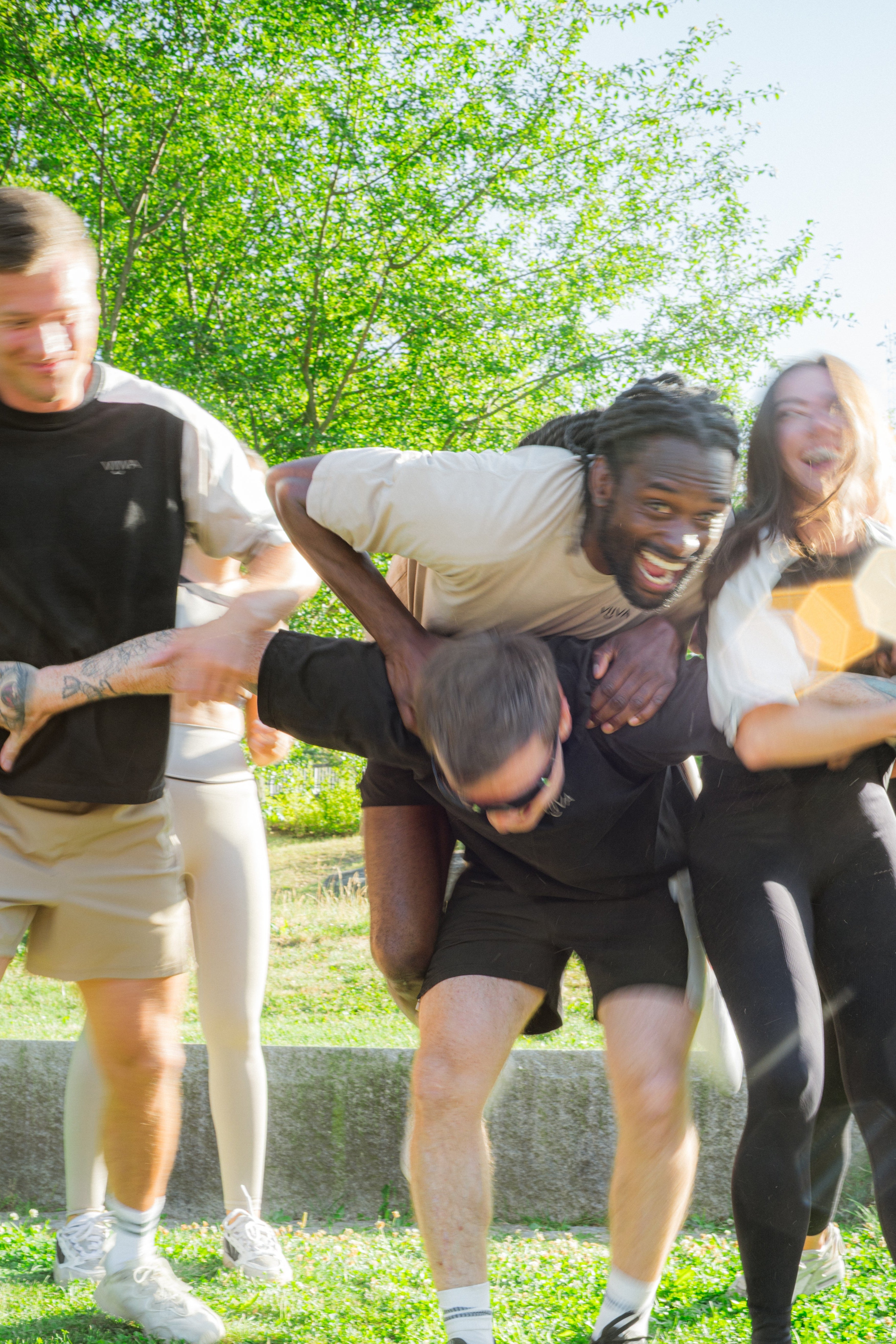 Group of people wearing activewear in neutral color, playing a game of human pyramid in a park
